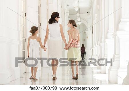 Stock Photo - Mother and daughter walking side by side holding hands, rear view. Fotosearch