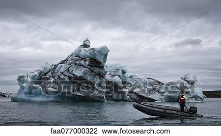 Stock Image - Motor boat moving past iceberg in Jokulsarlon glacial lagoon, Iceland. Fotosearch