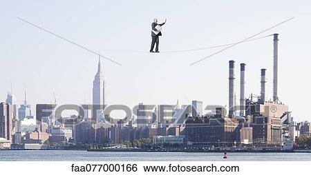 Stock Photograph - Oversized businessman walking on tightrope above city, carrying briefcase stuffed with cash. Fotosearch