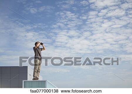 Stock Photo - Oversized man standing on rooftop, looking through binoculars. Fotosearch