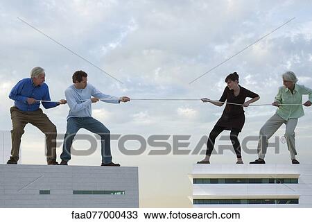 Stock Image - Oversized men and woman standing on rooftops, playing tug-of-war. Fotosearch