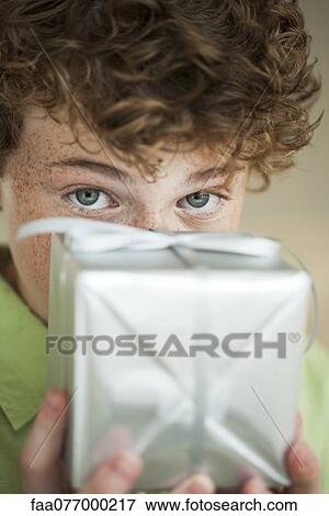 Stock Photo - Preteen boy holding wrapped gift in front of face. Fotosearch