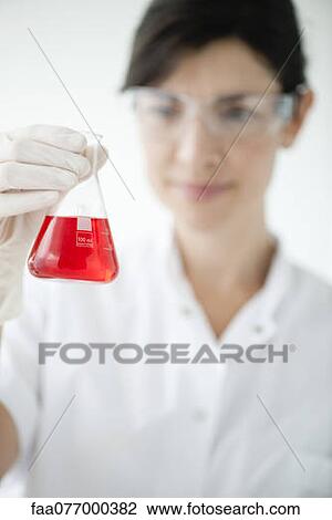 Stock Image - Scientist holding conical flask containing red liquid, focus on foreground. Fotosearch