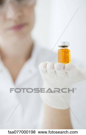 Stock Photo - Scientist holding vial containing orange liquid. Fotosearch