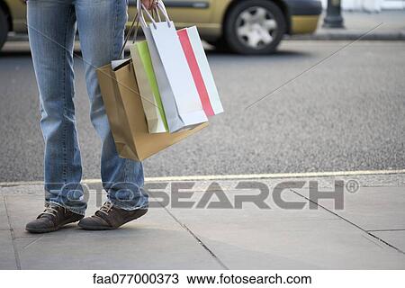 Stock Image - Shopper carrying shopping bags, low section. Fotosearch