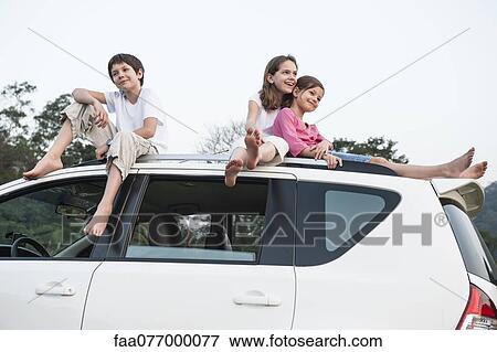 Stock Photo - Sibling sitting together on roof of car. Fotosearch