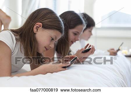 Siblings lying on bed playing handheld video games View Large Photo Image Stock Photo - Siblings lying on bed playing handheld video games. Fotosearch