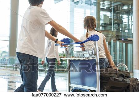 Stock Photo - Siblings pushing luggage cart in airport. Fotosearch