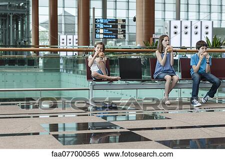 Stock Photography - Siblings sitting in airport eating sandwiches. Fotosearch