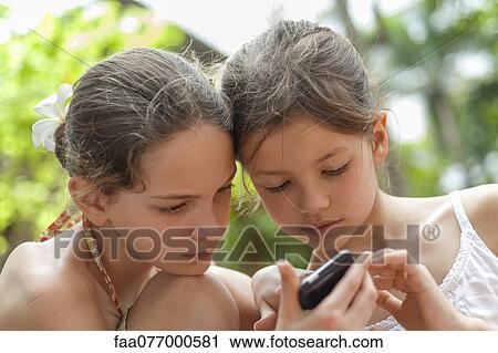 Stock Image - Sisters looking at cell phone together. Fotosearch