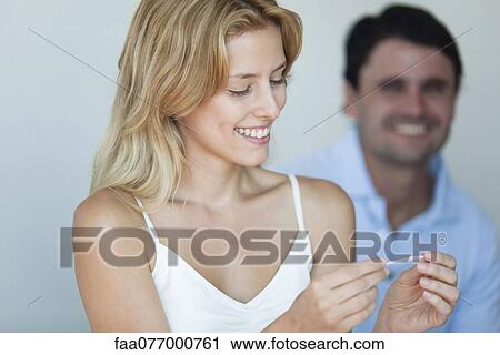 Smiling young woman holding pregnancy test, man in background View Large Photo Image Stock Image - Smiling young woman holding pregnancy test, man in background. Fotosearch