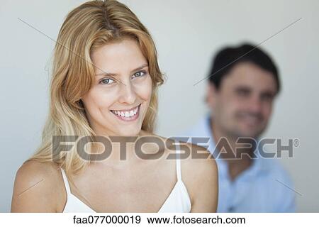Stock Photo - Smiling young woman in camisole, man in background. Fotosearch