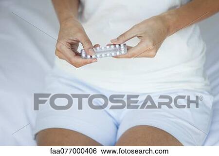 Stock Photograph - Woman holding birth control pills, mid section. Fotosearch