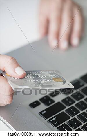 Stock Image - Woman holding credit card above laptop keyboard. Fotosearch