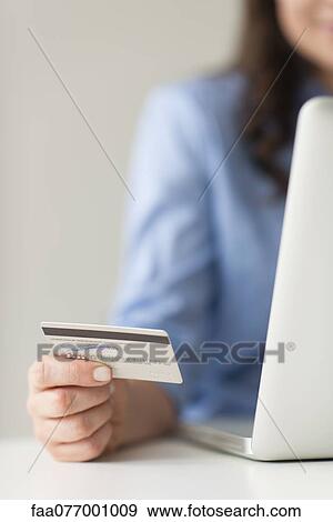 Woman holding credit card beside laptop computer View Large Photo Image Stock Photo - Woman holding credit card beside laptop computer. Fotosearch