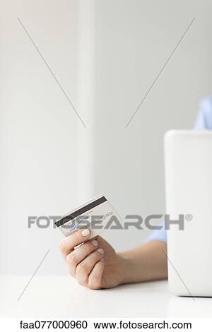 Stock Image - Woman holding credit card while using laptop computer, cropped. Fotosearch