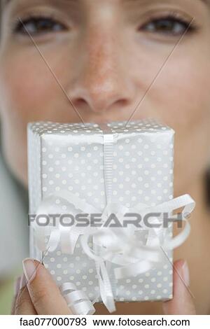 Stock Image - Woman holding gift in front of mouth, cropped. Fotosearch