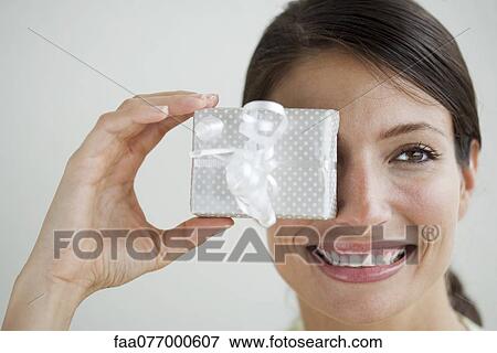 Woman holding gift in front of one eye View Large Photo Image Stock Photo - Woman holding gift in front of one eye. Fotosearch