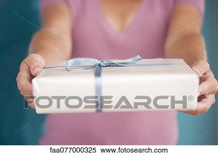 Stock Photography - Woman holding out wrapped gift, cropped. Fotosearch