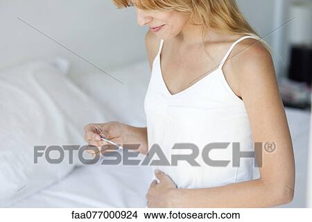 Picture - Woman holding pregnancy test on bed, smiling. Fotosearch