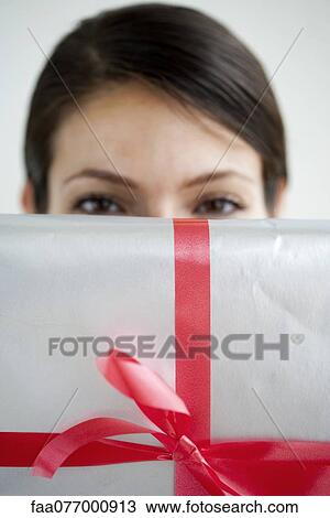 Woman holding wrapped gift in front of face View Large Photo Image Stock Image - Woman holding wrapped gift in front of face. Fotosearch