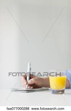 Stock Photo - Woman writing on notepad beside glass of orange juice. Fotosearch