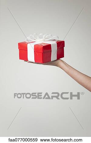 Stock Photo - Woman's arm holding out gift box, cropped. Fotosearch