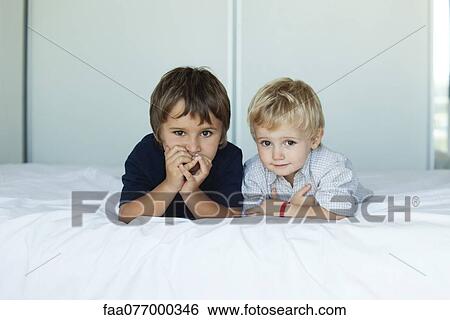 Stock Photograph - Young brothers lying on bed side by side, portrait. Fotosearch