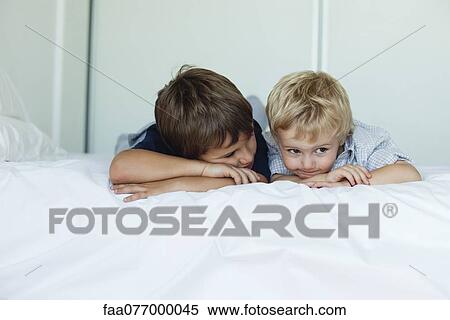Stock Photography - Young brothers lying on bed side by side, heads resting on arms. Fotosearch