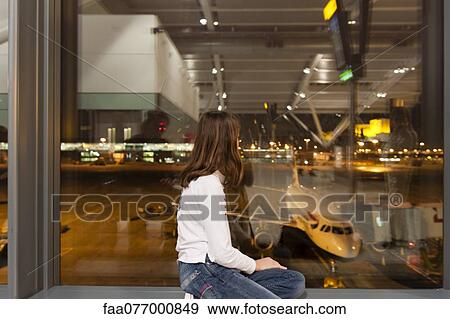 Stock Photo - Young girl watches from airport terminal window as flight crew prepare commercial airplane for boarding. Fotosearch
