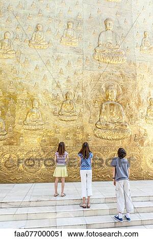 Stock Image - Young tourists looking up at Buddhist bas-relief. Fotosearch