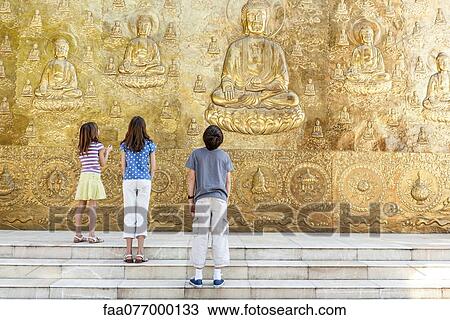 Stock Image - Young tourists looking up at Buddhist bas-relief. Fotosearch
