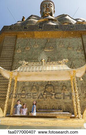 Stock Photo - Young tourists standing beneath large statue of buddha. Fotosearch