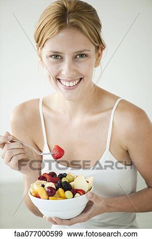 Young woman eating bowl of fruit, portrait View Large Photo Image Stock Photo - Young woman eating bowl of fruit, portrait. Fotosearch
