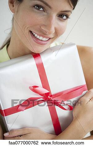 Stock Image - Young woman holding gift, portrait. Fotosearch