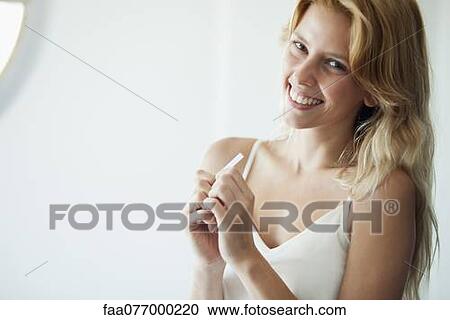 Stock Image - Young woman holding pregnancy test, smiling. Fotosearch