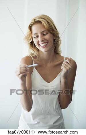 Stock Photo - Young woman holding pregnancy test, smiling. Fotosearch