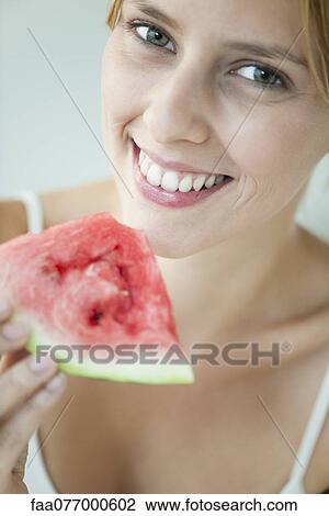 Stock Image - Young woman holding slice of watermelon, portrait. Fotosearch