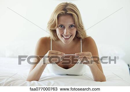 Young woman lying on bed holding pregnancy test View Large Photo Image Stock Image - Young woman lying on bed holding pregnancy test. Fotosearch