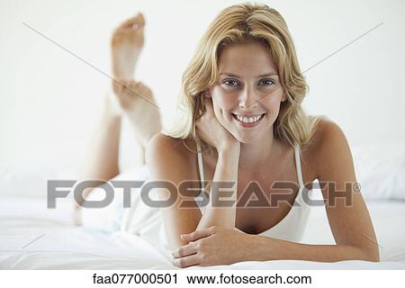 Stock Image - Young woman lying on bed. Fotosearch