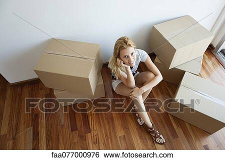 Stock Photograph - Young woman sitting on floor by cardboard boxes, high angle view. Fotosearch