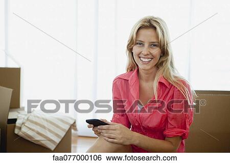 Stock Photograph - Young woman surrounded by cardboard boxes in new house, portrait. Fotosearch