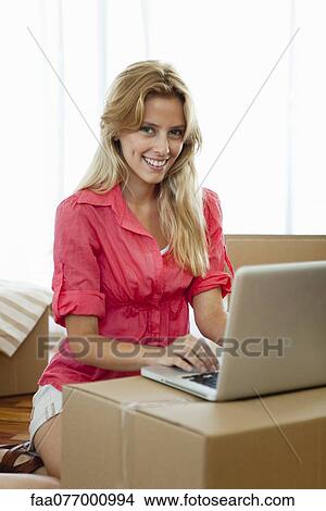 Picture - Young woman using laptop computer while surrounded by cardboard boxes. Fotosearch