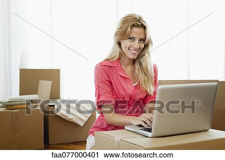 Young woman using laptop computer while surrounded by cardboard boxes View Large Photo Image Stock Image - Young woman using laptop computer while surrounded by cardboard boxes. Fotosearch