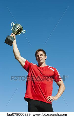 Stock Photo - Athlete holding up trophy. Fotosearch