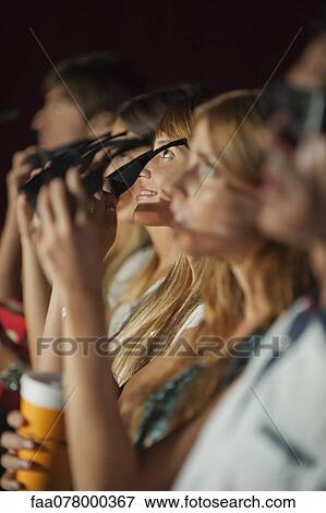Stock Photo - Audience in movie theater putting on 3-D glasses. Fotosearch