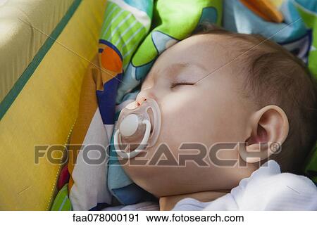 Stock Image - Baby girl napping with pacifier in her mouth. Fotosearch