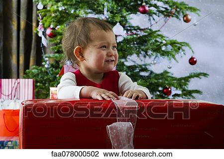 Stock Image - Baby girl opening large Christmas present. Fotosearch