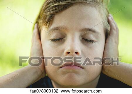 Stock Image - Boy covering ears with hands, eyes closed. Fotosearch