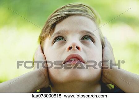 Stock Photography - Boy covering ears with hands, looking up. Fotosearch